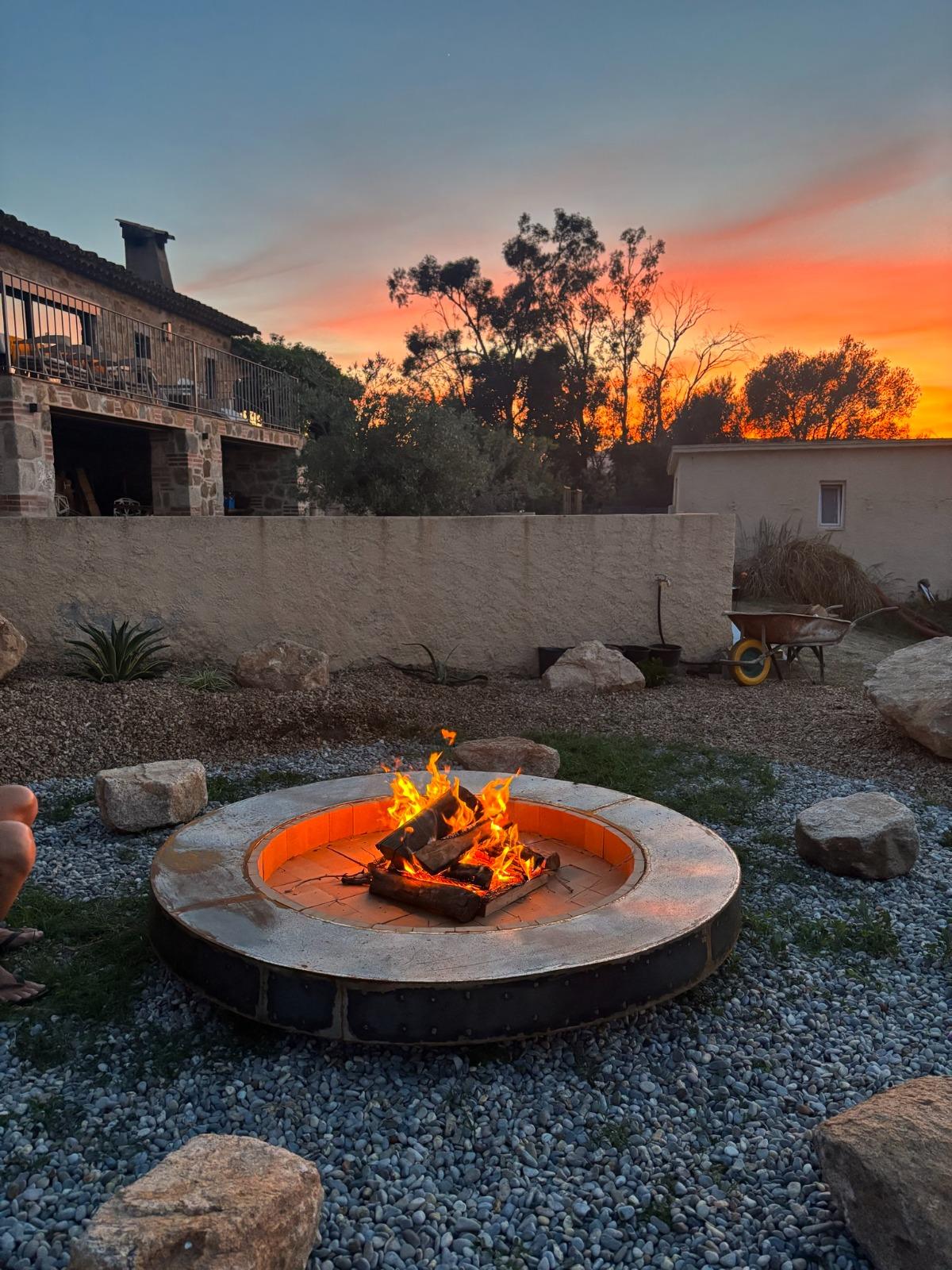 A stone fire pit lit at sunset in the Costa Brava garden, the farmhouse behind